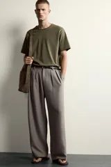 Pantalón relaxed fit de color blanco off-white, confeccionado en tejido con lino. Cuenta con pliegues frontales en la cintura, bolsillos delanteros y cierre frontal con cremallera y botón.