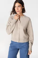 Saco tipo cardigan de punto color crudo, con cuello redondo, cierre frontal de botones y mangas largas con puños acanalados.