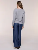 Buzo de punto fino color gris, de calce relajado, escote redondo amplio y canesú con textura acanalada. Cuenta con apliques de tachas metálicas doradas en la línea del hombro, mangas largas de hombro caído y puños y ruedo acanalados.