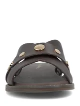 Sandalia plana color marrón oscuro, confeccionada en cuero, con tiras cruzadas en el empeine y tachas metálicas doradas decorativas.