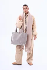 Bolso tipo shopper de gamuza en color gris, con detalles de tachuelas plateadas en los laterales. Cuenta con cierre superior y asas largas para llevar al hombro.