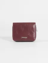 Billetera plegable color bordó con textura efecto cuero, cierre perimetral y placa metálica con logo en el frente.