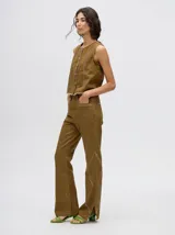 Pantalón de denim color marrón, de tiro alto y calce ochentoso con terminación estilo oxford. Cuenta con apliques metálicos decorativos alrededor de los bolsillos y a lo largo de las costuras exteriores.