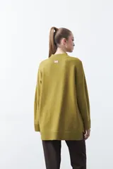 Polera de tejido de punto color marrón, con diseño asimétrico y costura diagonal frontal. Presenta cuello alto, hombros caídos, mangas largas con puños acanalados y ruedo con abertura frontal.