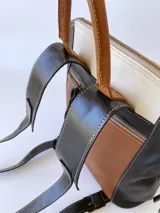 Mochila de cuero tricolor en tonos marrón tostado, negro y blanco, con bolsillo frontal con cierre, tiradores de cuero y detalle de etiqueta con logo grabado.