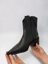 Bota texana de caña baja confeccionada en cuero genuino color negro, de inspiración western con puntera fina y tacón cuadrado. Cuenta con costuras decorativas en el empeine y cierre lateral.