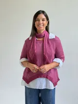 Sweater de punto color magenta con diseño asimétrico, cuello redondo y detalle de encaje bordado en el frente. Incluye una bufanda del mismo tejido y color, y se presenta superpuesto sobre una camisa blanca de algodón.