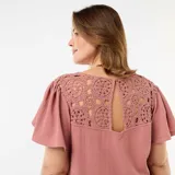 Camiseta rosada de manga corta con escote en V, confeccionada en tejido texturizado con detalles de encaje y macramé en los hombros.