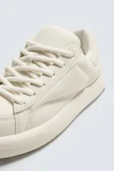 Zapatillas deportivas color crema, de cuero sintético, con cordones y suela de goma gruesa.