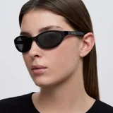 Lentes de sol con diseño cat-eye slim y envolvente, con montura y cristales en color negro.