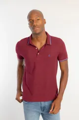 Camisa polo de manga corta en color bordó, confeccionada en tejido piquet. Presenta cuello y puños con detalles de frisos tricolor y cierre frontal con dos botones. Incluye un pequeño logo bordado en el pecho.