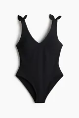 Malla enteriza de color negro con escote en V y breteles anchos con nudos decorativos en los hombros. Cuenta con copas con relleno extraíble y diseño completamente forrado.