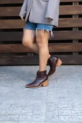 Botas cortas de cuero color marrón oscuro, con diseño estilo western, taco cuadrado de madera y punta fina.