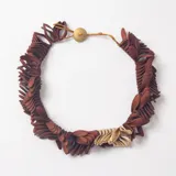 Collar de diseño artesanal compuesto por múltiples piezas pequeñas en forma de pétalos de color marrón, con un segmento de piezas en tono dorado y cierre de botón central.