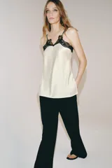 Top de tejido satinado color crema con escote en pico y tirantes finos. Presenta detalles de encaje negro en contraste en el escote y bajo recto.