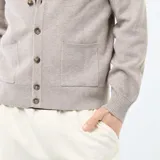 Cárdigan de punto color beige con cuello en V, cierre frontal con botones y dos bolsillos delanteros. Presenta puños y ruedo acanalados.