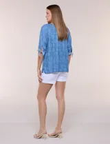 Blusa azul de lyocell con estampado floral, escote en V con bordado y aplique de cuentas de madera, mangas tres cuartos con lazos ajustables en los puños y diseño holgado.