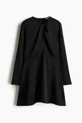 Vestido corto de color negro, con escote redondo y detalle girado en el frente. Presenta mangas largas con abertura en los puños, corte entallado en el torso y falda con leve vuelo. Cuenta con cierre oculto en la espalda.