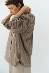 Camisa de popelina a rayas marrones, blancas y celestes, con cuello clásico, manga larga, bolsillo frontal de parche y cierre de botones.