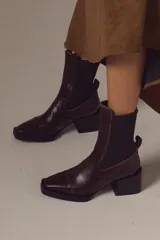 Bota tipo chelsea de cuero charolado color bordó, con caña media, elásticos laterales negros y taco cuadrado bajo.
