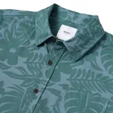 Camisa de manga corta con estampado de hojas y flores en tonos verde y celeste. Tiene cuello clásico, cierre con botones y bolsillo en el pecho.