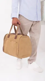 Bolso de lona color marrón claro con detalles en cuero marrón. Tiene apertura superior con cierre, bolsillos frontales y laterales con cierre, doble correa de mano con agarradera forrada y correa larga desmontable y regulable.