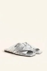 Sandalia tipo slide de cuero vacuno color blanco, con diseño de tiras cruzadas y fruncidas. Presenta una puntera cuadrada y una suela plana de cuero con un pequeño taco de 2 cm.