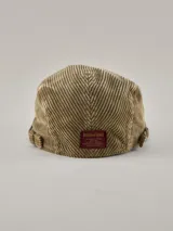 Boina tipo flat cap de pana color beige, con ajuste lateral mediante hebilla metálica.