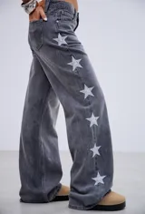 Jean de tiro medio en denim gris lavado, con corte recto y diseño de estrellas bordadas en color blanco a lo largo de los laterales externos de las piernas.