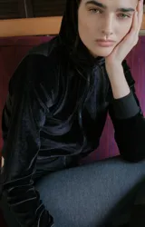 Campera negra de terciopelo con capucha, cierre frontal y bolsillos laterales.