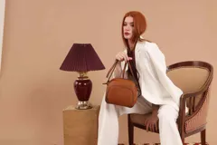 Bandolera de diseño compacto en color marrón claro, confeccionada en material símil cuero con textura granulada. Presenta un compartimento principal con cierre, un bolsillo frontal con cierre y correa regulable.