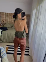 Chaleco top de cuero con efecto desgastado, escote halter profundo y cierre frontal con múltiples tiras para atar. Presenta bolsillos frontales aplicados con detalles de argollas metálicas.