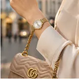 Reloj analógico de pulsera con caja y malla de acero en tono dorado, esfera clara con índices minimalistas y bisel con detalle de cristales.