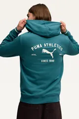 Canguro Puma modelo Class Graphic Hoodie, color crudo con capucha y bolsillo tipo canguro. Presenta un estampado en la espalda con el logo de la marca y la inscripción "Puma Athletics Since 1948".