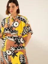 Vestido midi con estampado de piñas y motivos geométricos en tonos amarillo, marrón y negro. Presenta escote en V, mangas cortas y corte en la cintura con aberturas laterales.