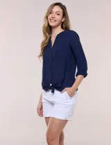 Blusa de calce relajado color salmón, confeccionada en tela liviana con textura sutil. Presenta escote en V con abotonadura frontal, bolsillo parche en el pecho, mangas largas regulables con presilla y ruedo con opción de anudar en el frente.