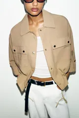 Chaqueta corta marrón de cuello solapa y manga remangada por debajo del codo. Presenta bolsillos delanteros de plastrón con solapa, bajo ajustable con cordón interior y cierre frontal con botones.