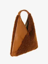 Cartera tipo hobo de gran tamaño, con forma envolvente y asa integrada. Presenta un diseño bicolor y de texturas mixtas: una sección es de cuero negro texturizado y la otra de material afelpado negro (tipo borrego o sherpa).