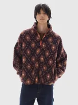 Campera de sherpa con estampado de rombos en tonos bordó, naranja y rosa. Presenta cuello alto, cierre frontal parcial con tirador naranja a contratono y bolsillos laterales.