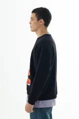 Buzo negro de algodón con cuello redondo y puños acanalados. Estampado frontal con un personaje de caricatura y el texto "HOME ALONE" en verde.