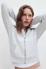 Chaqueta de felpa color gris claro melange, con cuello solapa, manga larga con puños elastizados, bolsillos frontales y cierre de cremallera completa.