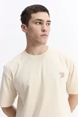 Remera de manga corta color crema con cuello redondo y fit regular. Presenta un estampado grande en la espalda con una flor estilizada en tonos rojo y azul, y texto que incluye "WE ALL GROW" y "trust the process, great things take time".