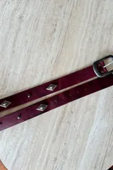 Cinturón de cuero vacuno color bordó con apliques metálicos en forma de rombo y hebilla metálica rectangular.