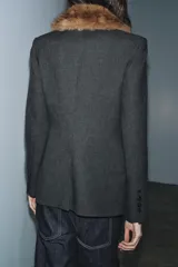 Blazer entallada de color gris oscuro, confeccionada en tejido con algodón. Presenta un cuello solapa con aplicación de pelo sintético desmontable, manga larga, bolsillos delanteros con solapa y cierre frontal con botones.