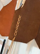 Chaleco artesanal confeccionado en cuero, con diseño de cordones decorativos en el frente y terminaciones rústicas.