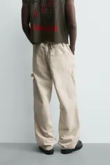 Pantalón relaxed fit color beige, confeccionado en tejido de algodón. Cuenta con bolsillos frontales, bolsillos traseros de plastrón y aplicación de bolsillos plastrón con tira multifunción en la pernera. Cierre frontal con cremallera y botón.