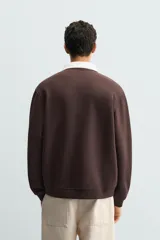 Sudadera tipo polo de corte regular, color gris claro, con cuello solapa en color blanco y cierre frontal de botonadura oculta. Presenta mangas largas con puños y ruedo en rib.