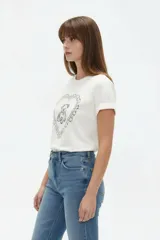 Remera de algodón color beige, de manga corta con vuelta, cuello redondo y estampa frontal de flores con lazo en tonos azules y celestes.