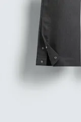 Pantalón de vestir gris oscuro, corte ancho (flare fit) y tiro alto, con bolsillos laterales y falsos bolsillos de vivo en la parte trasera. Presenta un cierre frontal con cremallera y gancho oculto, y botones a presión ocultos en el bajo.