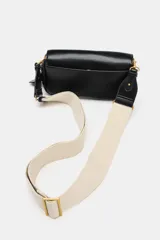 Bolso bandolera de formato alargado en color negro, con solapa frontal y cierre metálico. Incluye una correa ajustable de tejido en color crudo y herrajes dorados.